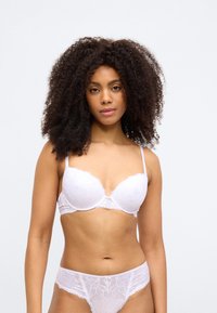 Bielizeň biely čipkovaný podprsenka s kosticami a nastaviteľnými ramienkami, doplnená zhodnými čipkovanými tangami. Ozdobená kvetinovými vzormi a jemnými lemami.