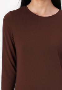 Bluza maro cu mânecă lungă, confecționată dintr-un material moale, având un decolteu rotund și un design fără cusături la umeri. Textură netedă, siluetă ajustată.