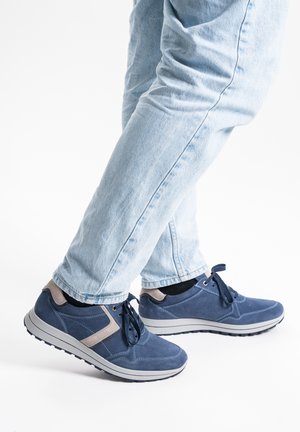 Blaue Wildleder-Sneaker mit grauen Akzenten, Schnürung und strukturierten Sohlen, kombiniert mit hellblauen Jeans, seitlich positioniert.