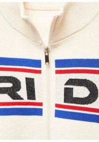 Krémový svetr na zip s žebrovaným límcem, který má velkou grafiku v černých, červených a modrých pruzích. Stříbrný zip v přední části.