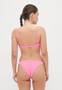 Rožinė bikinio komplektas su grioveliais, reguliuojamomis petnešėlėmis ir nugaros uždarymu. Turi paprastą dizainą su minimaliais aksesuarais ir tekstūruotu paviršiumi.