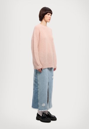 Rosa strikkegenser, løs passform, med en myk tekstur. Kombinert med en lyseblå denimskjørt med slitte detaljer og en front splitt. Svarte sko.