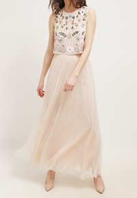 Beige maxiklänning med ärmlös broderad överdel med blommönster och en plisserad, flödande chiffongkjol. Elegant och lätt.