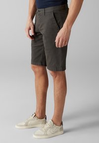 Shorts en coton gris foncé avec une coupe droite, poches avant et fermeture par bouton à la taille, associés à des baskets beiges basse.