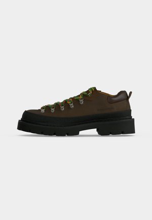 Chaussure de randonnée en cuir marron avec une semelle noire épaisse et des lacets verts et orange à motifs sur un fond blanc uni.