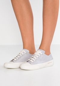 Šedé semišové tenisky s bílými gumovými podrážkami a tkaničkami, s nízkým střihem a jemným brandingem na boku.