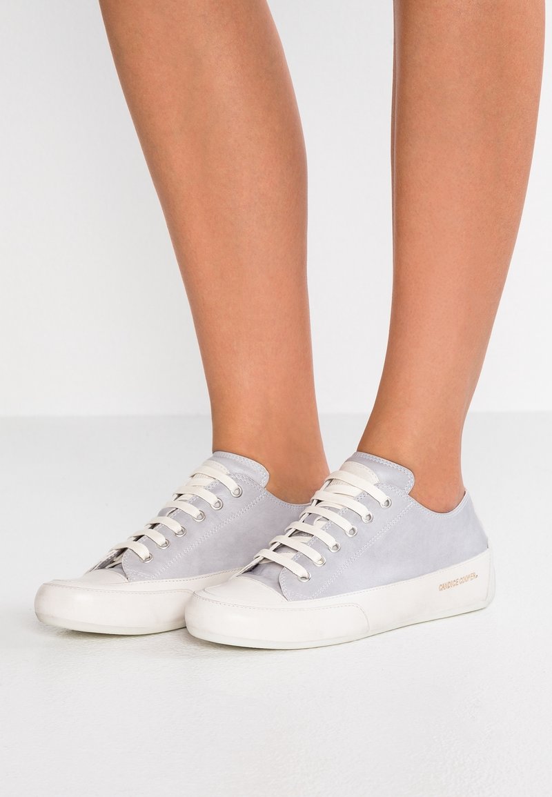 Šedé semišové tenisky s bílými gumovými podrážkami a tkaničkami, s nízkým střihem a jemným brandingem na boku.