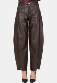 Pantaloni marroni in similpelle a vita alta con gamba larga, tasche frontali e chiusura con bottone, indossati con tacchi neri a punta e top bordeaux.