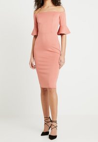 Off-shoulder, figurerande midiklänning i mjuk rosa med trumpetärmar. Slät tyg, lätt lyster och knälång längd. Svarta snörskor.