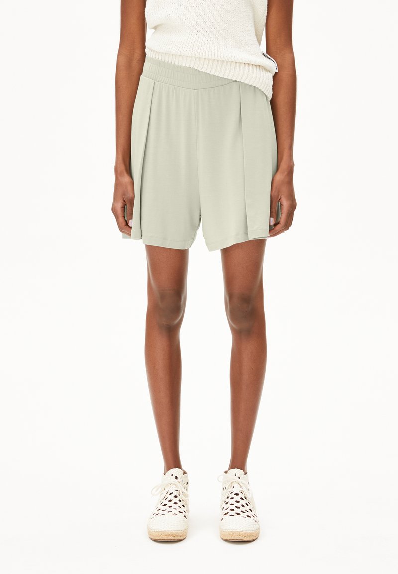Hellgrüne, plissierte Shorts mit einem elastischen Bund, aus weichem Stoff gefertigt. Kombiniert mit weißen Schnürsneakern mit einer natürlichen Sohle.