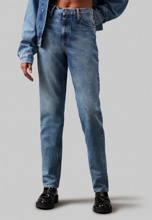 Light blue denim jeans with a straight leg cut, button closure, five-pocket design, and subtle fading. Paired with black lace-up shoes.