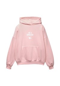 Un sweatshirt rose clair avec une poche avant et un texte blanc "DANS UN RÊVE Reste sauvage, reste étrange" au-dessus d'un graphique d'étoile sur la poitrine.