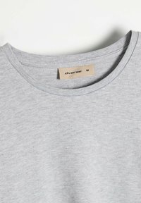 Szara koszulka z okrągłym dekoltem z miękkiej bawełny, z prostym wzornictwem oraz małą metką z nazwą marki i rozmiarem M.