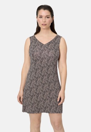 Mujer de cabello oscuro que lleva un vestido corto sin mangas con un patrón abstracto en negro y rosa claro, de pie contra un fondo liso y claro.