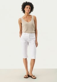 Débardeur en tricot beige avec un col en V, associé à un pantalon blanc raccourci et des tongs marron. Design simple et ajusté sans motifs.