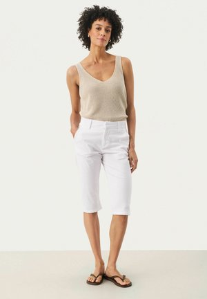 Top in maglia beige con scollo a V, abbinato a pantaloni bianchi a vita alta e infradito marroni. Design semplice e aderente, senza motivi.