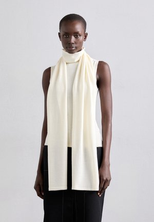 Écharpe de couleur crème drapée autour d'un haut sans manches, faite d'un tissu doux. L'écharpe a une finition nette, sans motifs ni embellissements.