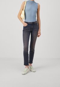 Ljusblå ärmlös topp, mörkblå jeans med viss förslitning och vita sneakers med gröna accenter, tillsammans med en liten gul handväska.