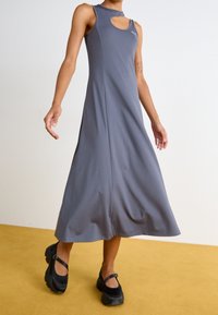 Robe grise sans manches avec un décolleté rond découpé et une silhouette évasée en ligne A. Associée à des chaussures à plateforme noires. Tissu à texture lisse.