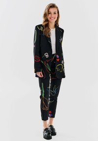 Czarny garnitur z wielokolorowym haftem kwiatowym, składający się z dopasowanej marynarki i slim-fit spodni. W połączeniu z czarnymi platformowymi loafersami.