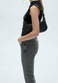 Czarna skórzana torba na ramię o zaokrąglonym kształcie, z regulowanym paskiem i teksturowaną powierzchnią, zestawiona z dopasowanymi szarymi dżinsami i czarnym topem.