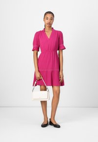 Fuchsia jurk met korte pofmouwen en een v-hals, met een kanten rand bij de taille. Gecombineerd met een witte handtas en zwarte ballerina's.