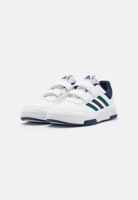 Baskets de sport blanches avec des accents verts et marine, tige synthétique texturée, deux bandes Velcro et semelle en caoutchouc avec un motif en chevrons.