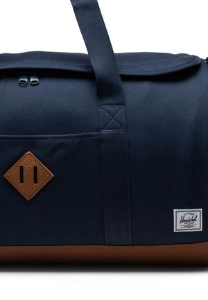 Navy fabric duffel bag with brown leather accents, featuring a rectangular shape, top zip closure, and a small brand label.