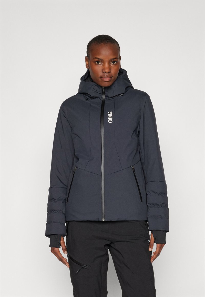 Dunkelblauer Pufferjacke mit Reißverschluss vorne, verstellbare Kapuze und Seitentaschen. Mit einem Logo auf der Brust und strukturierten Ärmeln.