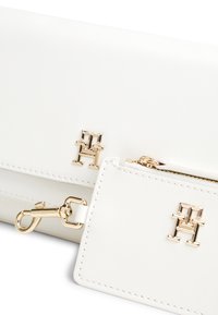 Λευκό δερμάτινο πορτοφόλι με επιχρυσωμένα μεταλλικά στοιχεία, διαθέτει εμφανές λογότυπο και αφαιρούμενη θήκη καρτών με κοκκάλινο κλιπ. Ομαλή υφή, κλείσιμο με φερμουάρ.