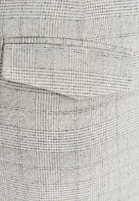 Szara tkanina w kratkę z cienkimi czarnymi liniami. Zawiera widoczną klapę kieszeni, teksturowany splot i subtelny wzór w kratę.