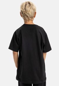 Čierne bavlnené tričko s krátkymi rukávmi, voľný strih a okrúhlym výstrihom. Viditeľné šitie na leme a rukávoch. Bez grafiky alebo vzorov.