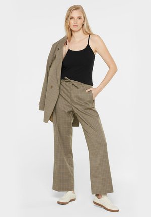 Braune karierte Hose mit entspannter Passform, hohem Bund und passendem Blazer, kombiniert mit einem schwarzen Top und weißen Sneakers.