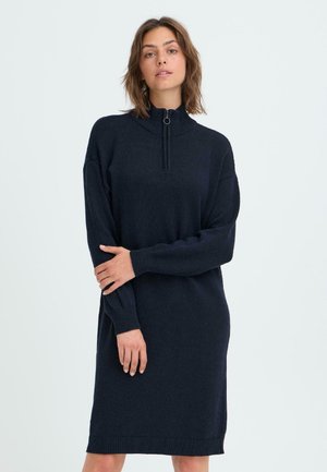 Marinblå stickad klänning med hög krage, dragkedja i nacken, långa ärmar samt ribbade manschetter och nederdel. Mjuk textur och avslappnad passform.