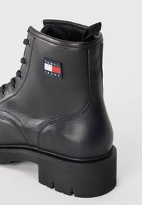 Bottes chelsea en cuir noir avec une semelle en caoutchouc épaisse, arborant un patch logo Tommy Jeans en rouge, blanc et bleu sur le côté extérieur.