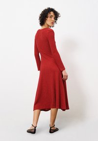 Rotes Langarmkleid mit tailliertem Oberteil und weit ausgestellt Rock, aus einem strukturierten Material gefertigt, mittellang bis zur Wade und mit rundem Halsausschnitt.