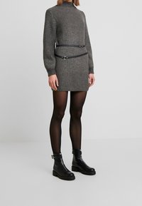 Abito grigio a maglia con un collo alto, design con cintura e maniche lunghe, abbinato a stivaletti neri e collant neri trasparenti.