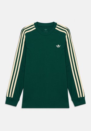 Cămașă verde închis cu mâneci lungi, cu trei dungi bej de-a lungul mânecilor și logo mic Adidas pe pieptul stâng.