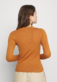 Pull en ribbed orange à manches longues et col rond. Doté d'accents aux épaules et d'une coupe ajustée, fabriqué dans un matériau doux et élastique.