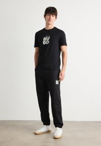 Černé bavlněné tričko a odpovídající tepláky, s bílým logem "HUGO". Bílé tenisky s béžovými akcenty. Jednoduchý, moderní design.