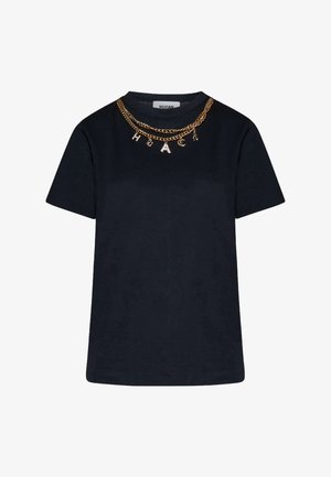 Maglietta nera a maniche corte con due collane a catena dorate che presentano ciondoli a lettere che formano la parola "HACK" intorno al colletto.