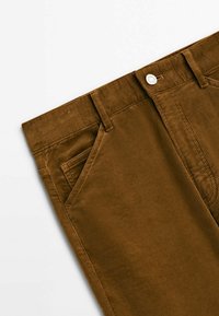 Pantalon en velours côtelé marron avec une surface texturée, doté d'une taille standard, de deux poches avant et d'une fermeture par bouton métallique.