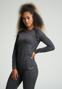 Dunkelgraues langärmliges Sportoberteil mit strukturierten Seitenelementen und subtilen Fischgrätmustern. Präsentiert mit passenden Leggings.