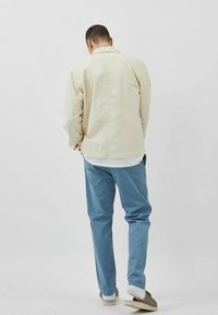 Veste beige clair avec un col, associée à un pantalon bleu clair. La veste a une coupe décontractée, et le pantalon est fuselé avec une texture lisse.