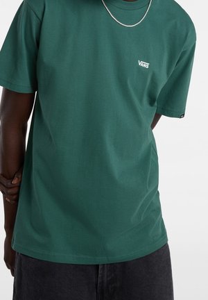 Zielona bawełniana koszulka z krótkimi rękawami, z małym białym logo Vans na piersi i prostym dołem. Tekstura wydaje się gładka.