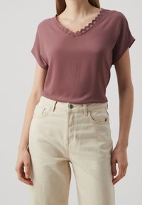 Kortärmad topp med v-ringning i dämpad rosaton med vågig halsringning, i kombination med högmidjade beiga jeans. Slät textur, avslappnad passform.