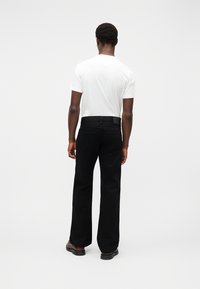 Μαύρο παντελόνι φαρδιάς γραμμής με απαλή υφή, συνδυασμένο με απλό λευκό μπλουζάκι, με στάνταρντ σχεδιασμό πίσω τσέπης.