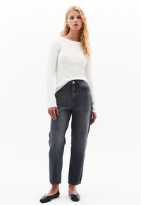 Vit långärmad skjorta tillsammans med mörkgrå högmidjade jeans i denim. Looken har en avslappnad passform och svarta platta skor.