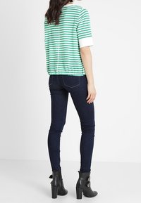 Zielona i biała w paski bluzka z krótkim rękawem i elastycznym dołem, w połączeniu z ciemnymi skinny jeansami i czarnymi botkami na obcasie z akcentami klamry.