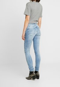 Jeans skinny blu con una finitura sbiadita, design a cinque tasche e lavaggio chiaro, abbinati a una t-shirt grigia e stivaletti neri con tacco.